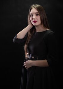 Anna Zborowska w czarnej sukience z dłonią przy twarzy, ciemne tło