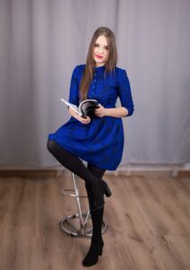 Anna Zborowska z książką na wysokim stołku, cała postać, szare tło
