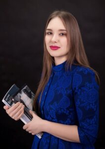 Anna Zborowska w kobaltowej sukience z książkami w dłoni, ciemne tło