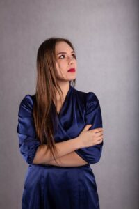 Anna Zborowska w granatowej sukience z rękami skrzyżowanymi, szare tło