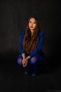 Anna Zborowska w kobaltowej sukience, siedząca, cała postać