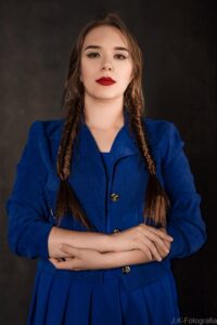 Anna Zborowska w kobaltowej sukience z warkoczami, ciemne tło