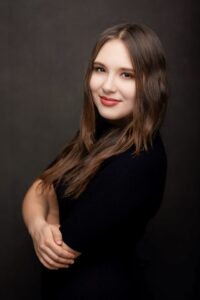 Anna Zborowska w czarnej bluzce z dłonią na ramieniu