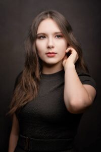 Anna Zborowska w czarnej bluzce z dłonią we włosach