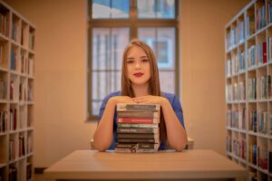 Anna Zborowska przy stole ze stosem książek w bibliotece