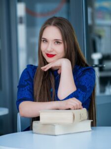 Anna Zborowska w kobaltowej sukience oparta o książki