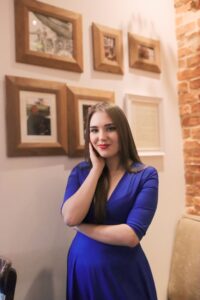 Anna Zborowska przy stoliku w kawiarni, ramki na ścianie
